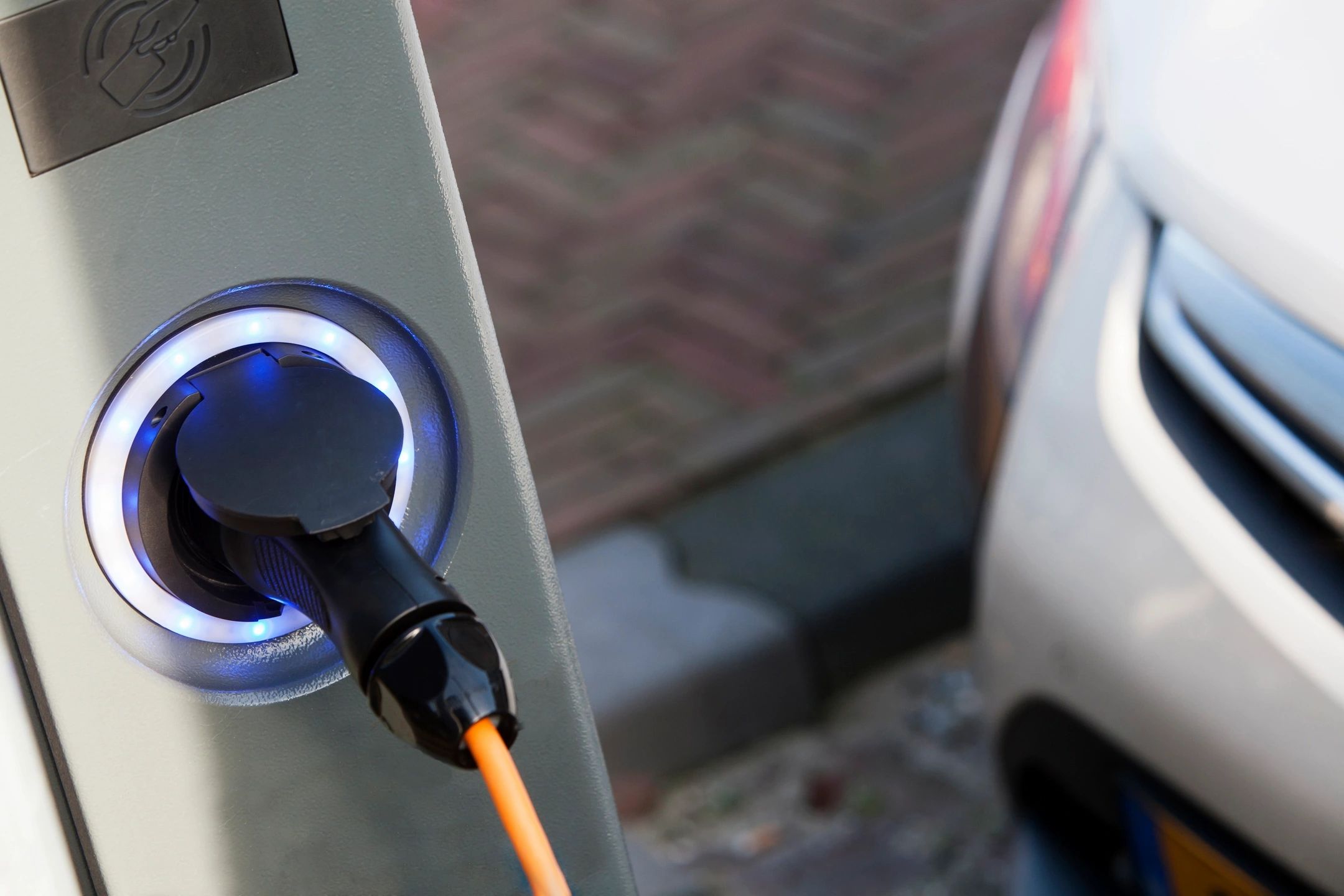 Electric vehicle charging station with a car connected to a charging cable outdoors.