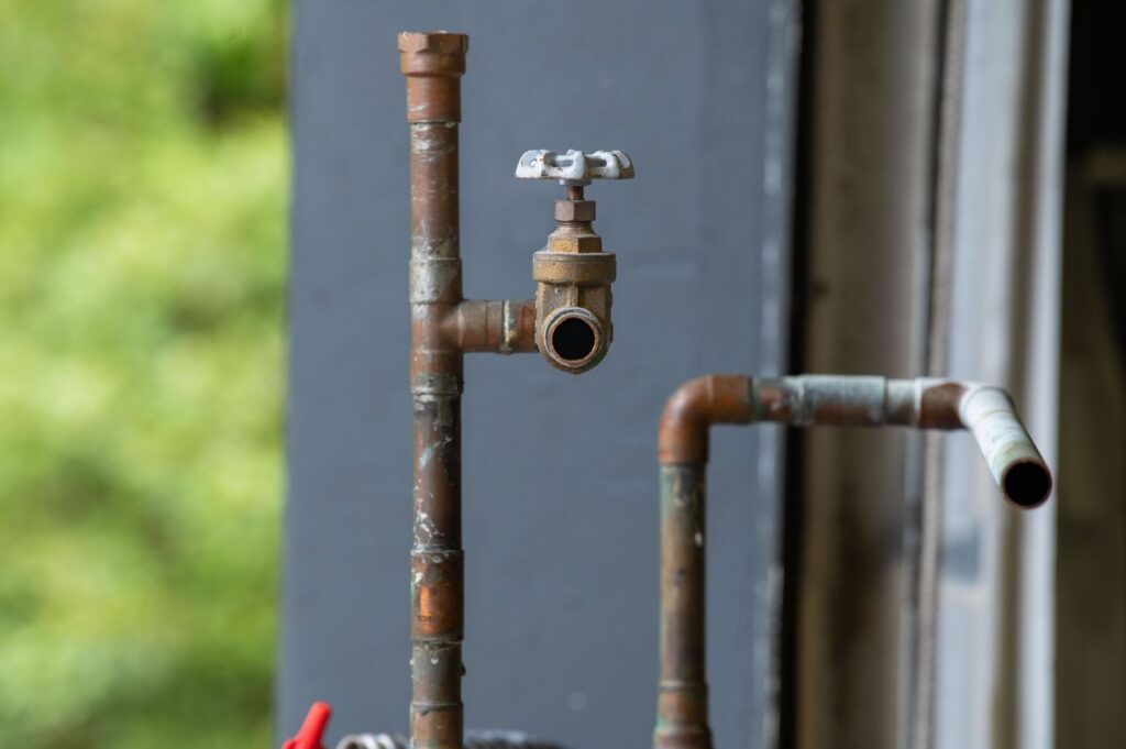 Close up of corroded and rusty copper water pipes with an aging shutoff valve, a common sign a home needs repiping