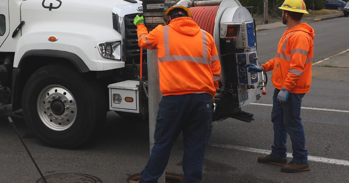 Hydro jetting hose reel and crew jetting a sewer line through a street manhole