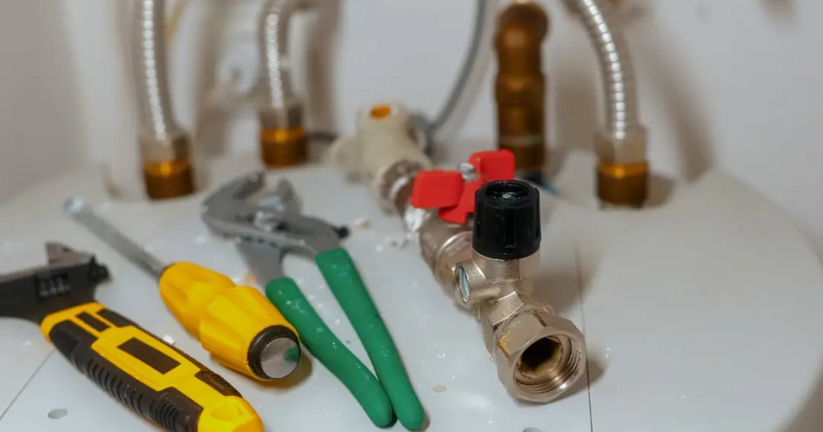 Storage tank water heater during installation, showing new flex connectors, shutoff valve, and plumber tools on top of the tank
