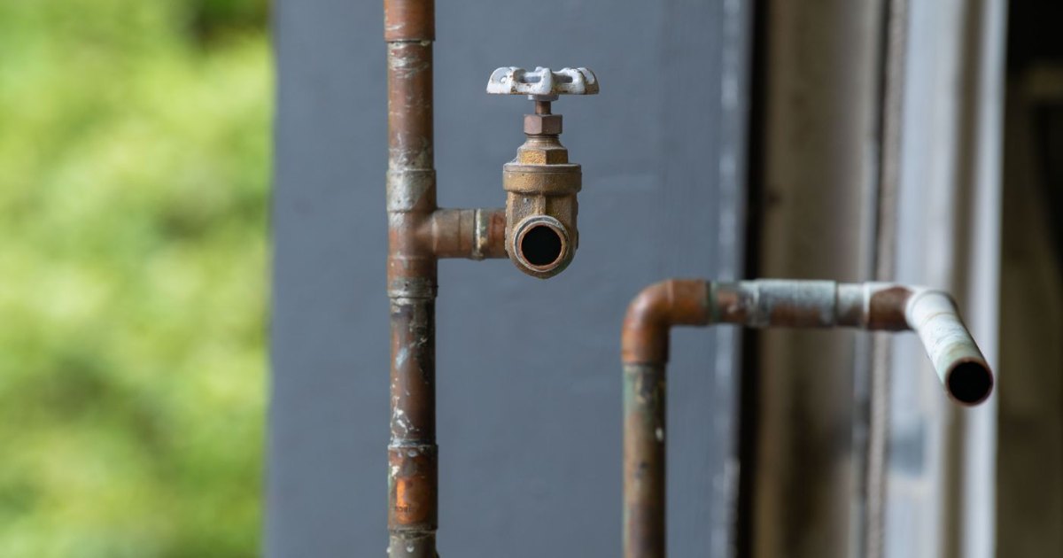 Aging copper water pipes and a shutoff valve showing corrosion, the type of pipe wear behind many slab leaks
